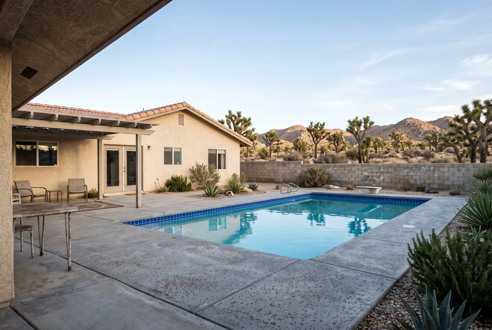 Backyard pool with bright blue waterline tile and Joshua trees beyond the wall